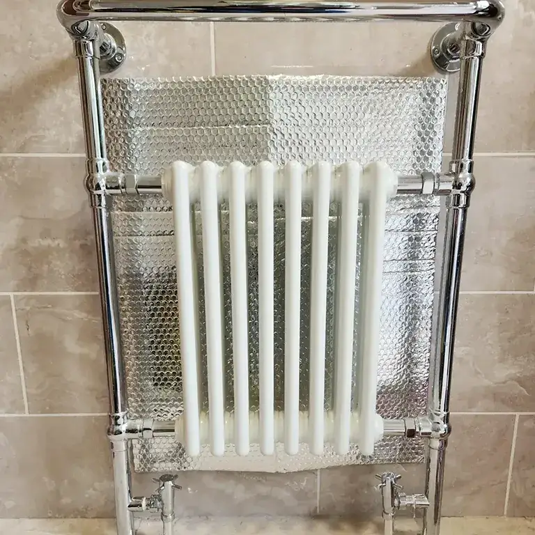A white radiator in a bathroom next to a tiled wall.